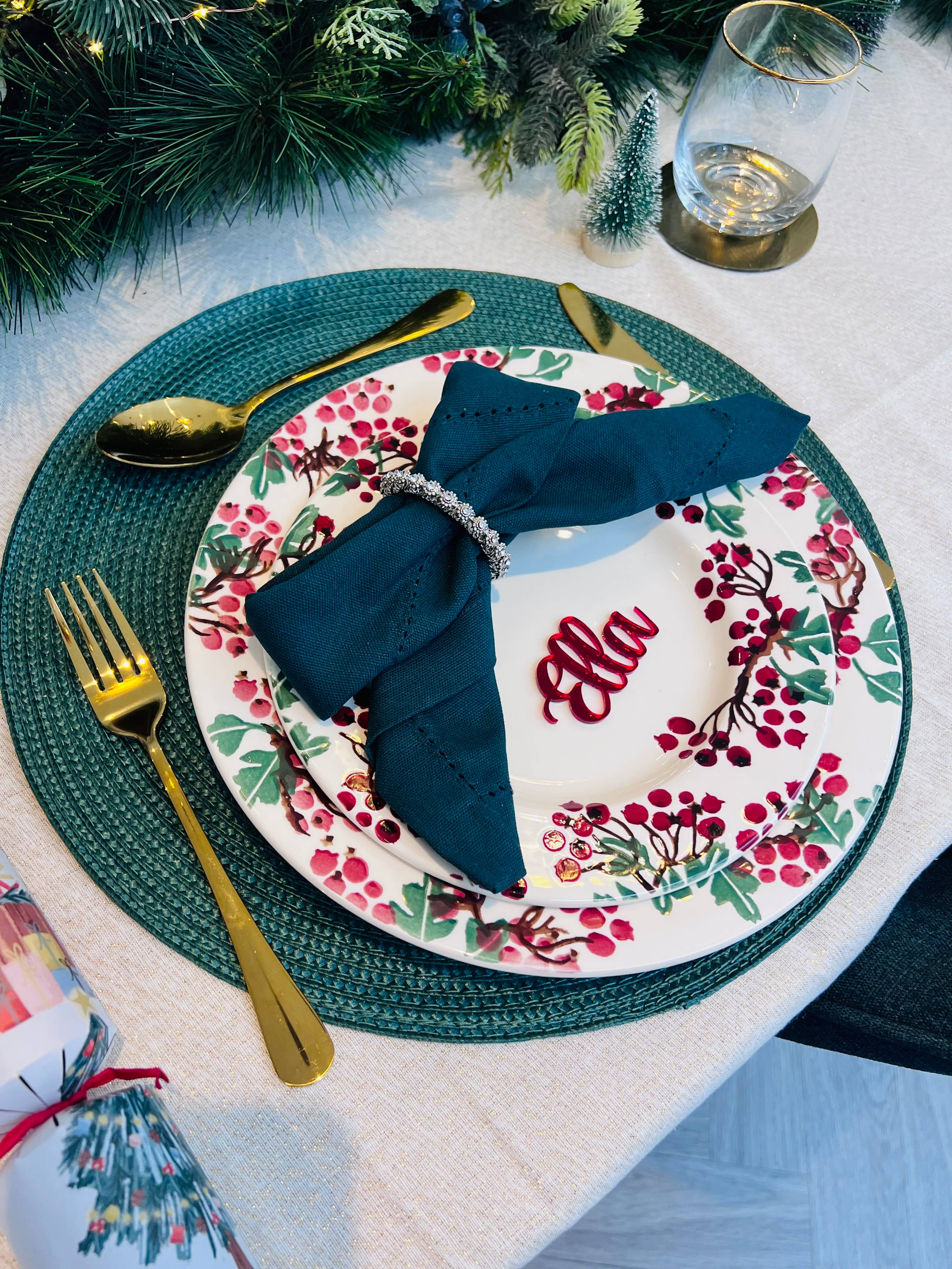 Christmas dinner table setting with personalised acrylic place name ‘Ella’ in red, festive plate and green napkin